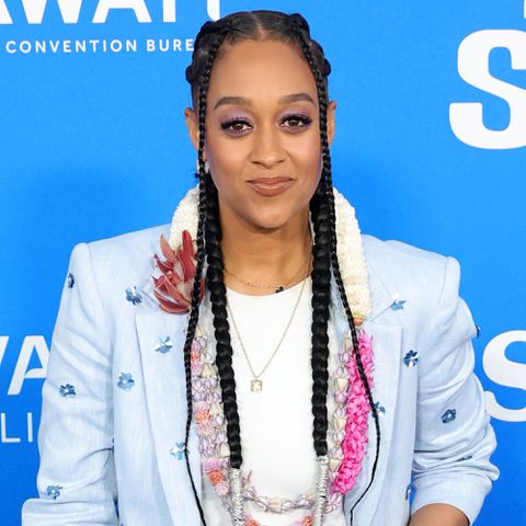 Tia Mowry attending an event, wearing a light-colored outfit with intricate details and standing against a blue backdrop Kevin Winter/WireImage Tia Mowry